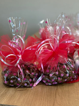 Bags of chocolate covered treats with pink ribbons on a wooden surface