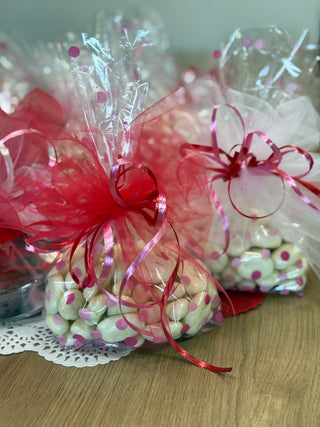 Bouquets of candy in clear cellophane bags with red ribbons on a wooden surface.