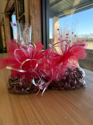 Two clear gift bags with pink ribbons and polka dots on a wooden surface.