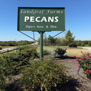 Sign for Landgraf Farms Pecans with a scenic background of trees and flowers.